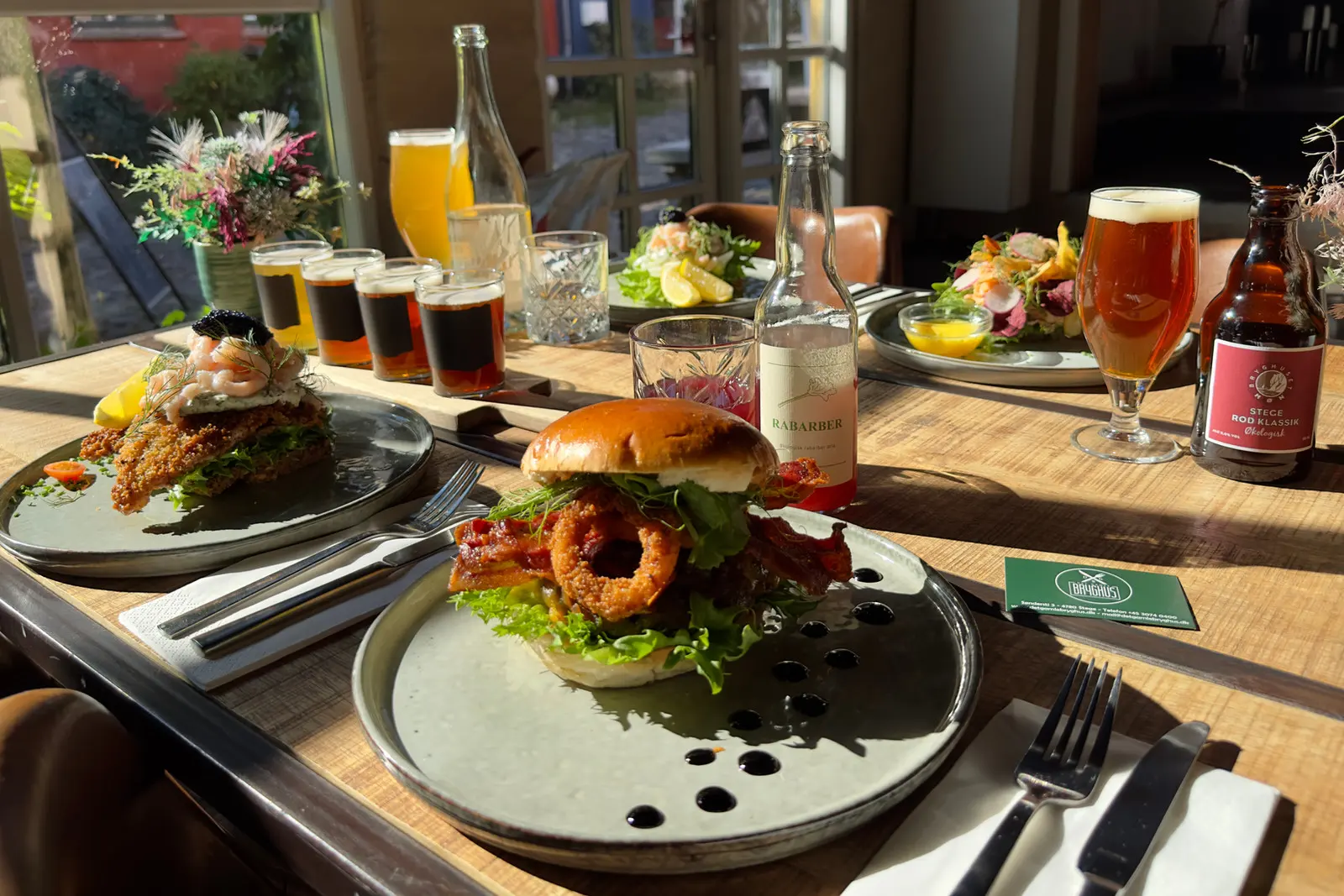 Burger med løgringe og fadøl på et solbeskinnet bord ved vinduet